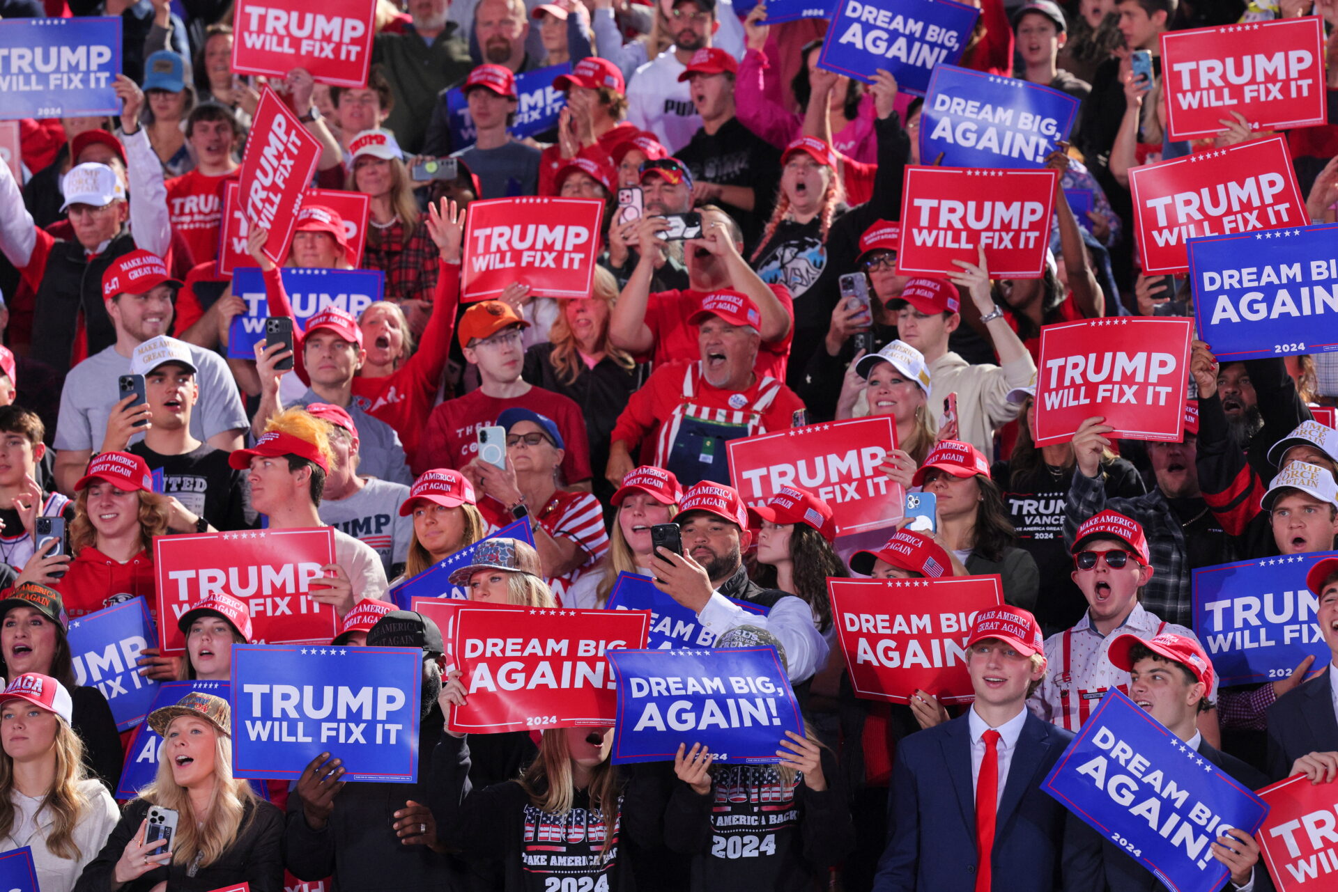 Eine begeisterte Menge von Unterstützern mit Schildern wie „Trump will fix it“ und „Dream Big Again!“ bei einer Wahlkampfveranstaltung für Donald Trump im Jahr 2024.